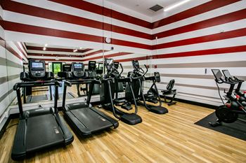 a gym with cardio equipment and a red and white wall